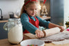 child rolling out cookie dough in kitchen wearing Christmas headband