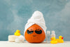 orange pumpkin with drawn on closed eyes and a smile, wearing a white towel hat and black under-eye masks, blue background