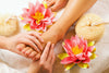 woman getting a foot massage surrounded by pink and yellow flowers.