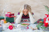 woman looking extremely stressed as she sits at a table covered in Christmas gifts and wrapping paper.