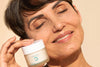 older woman smiling with her eyes closed and holding up Noche's Ocean Caviar Anti-Wrinkle Face Cream.