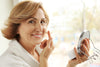 senior woman smiling at the camera as she applies moisturizer to her face.